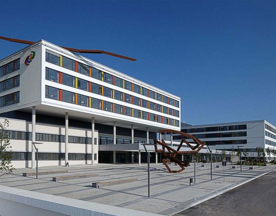 Modern hospital building with colorful window accents, outdoor sculptures, and clear blue sky.