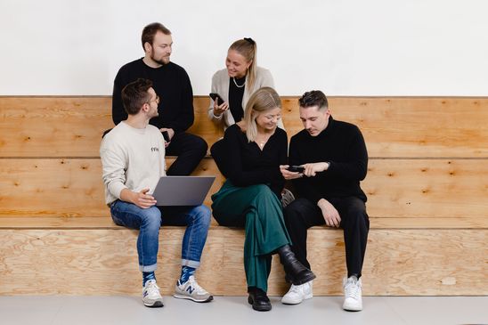 Five people on wooden steps collaborating with laptop and phone, symbolizing employee engagement.