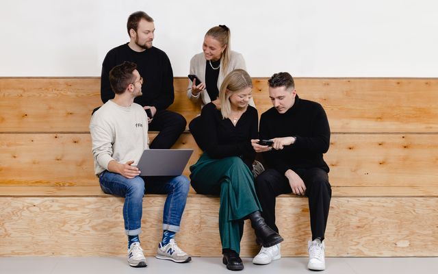 Five people on wooden steps collaborating with laptop and phone, symbolizing employee engagement.