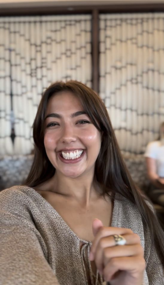 Smiling person indoors with patterned background.