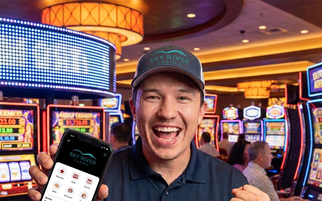 Man in Sky River Casino shirt holding phone displaying app.
