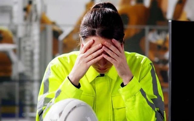 Worker in high-vis jacket with head in hands, hard hat on table.