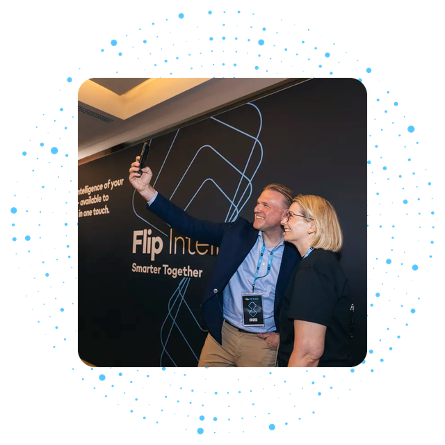 Two people taking a selfie at a Flip event with a backdrop reading Flip Int... Smarter Together.