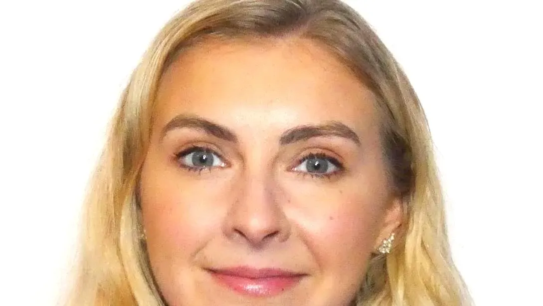 Portrait of a woman with long blonde hair, pink top, and neutral background.