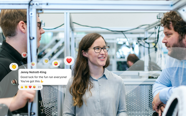 Three people in a tech lab setting, engaged in conversation. A social media message overlay reads, "Good luck for the fun run everyone! You've got this 👍."