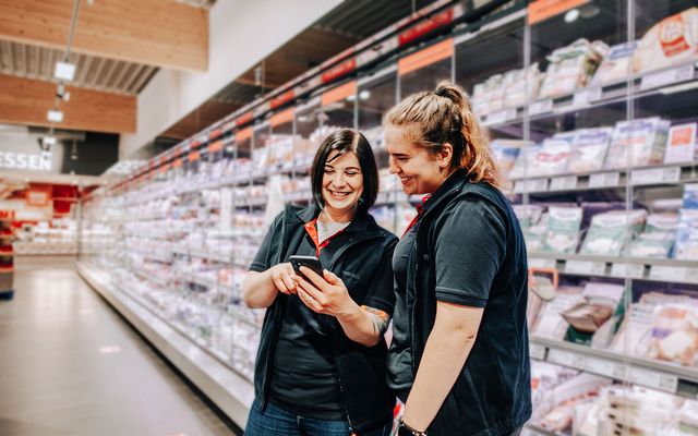 Two Mitarbeiterinnen nutzen eine Mitarbeiter App für Employee Experience und Engagement im Supermarkt.