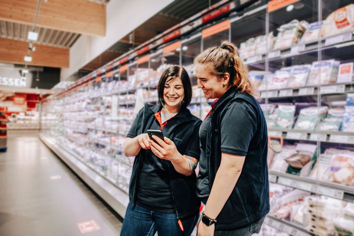 Two Mitarbeiterinnen nutzen eine Mitarbeiter App für Employee Experience und Engagement im Supermarkt.