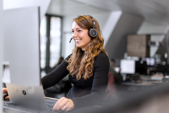 Smiling woman uses headset and computer in office, empowering frontline via Mitarbeiter App, HR-Portal.