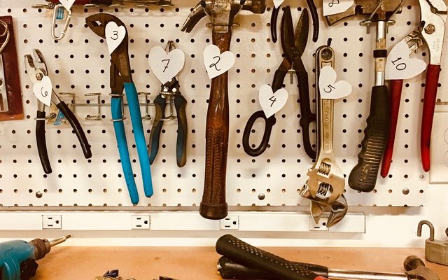 Various hand tools, including pliers, hammers, and wrenches, hang on a pegboard, each labeled with a numbered heart-shaped ta