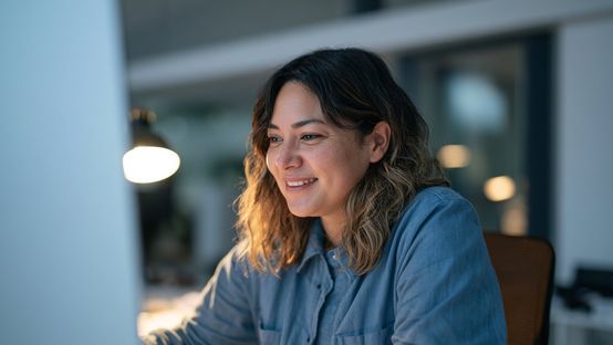 Person smiling while working on a computer in an office.