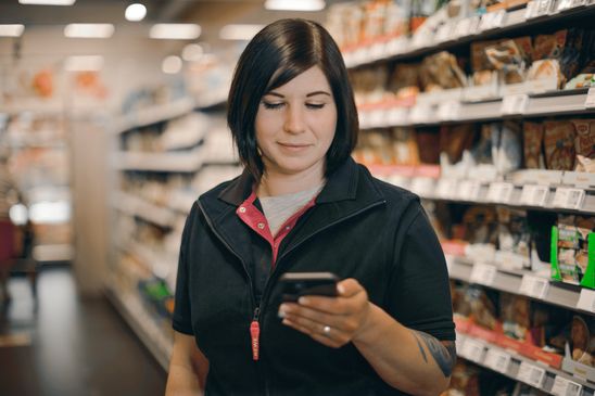 Woman in supermarket aisle using smartphone, representing empowered frontline retail employee.