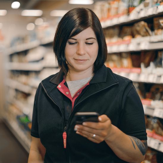 Woman in supermarket aisle using smartphone, representing empowered frontline retail employee.