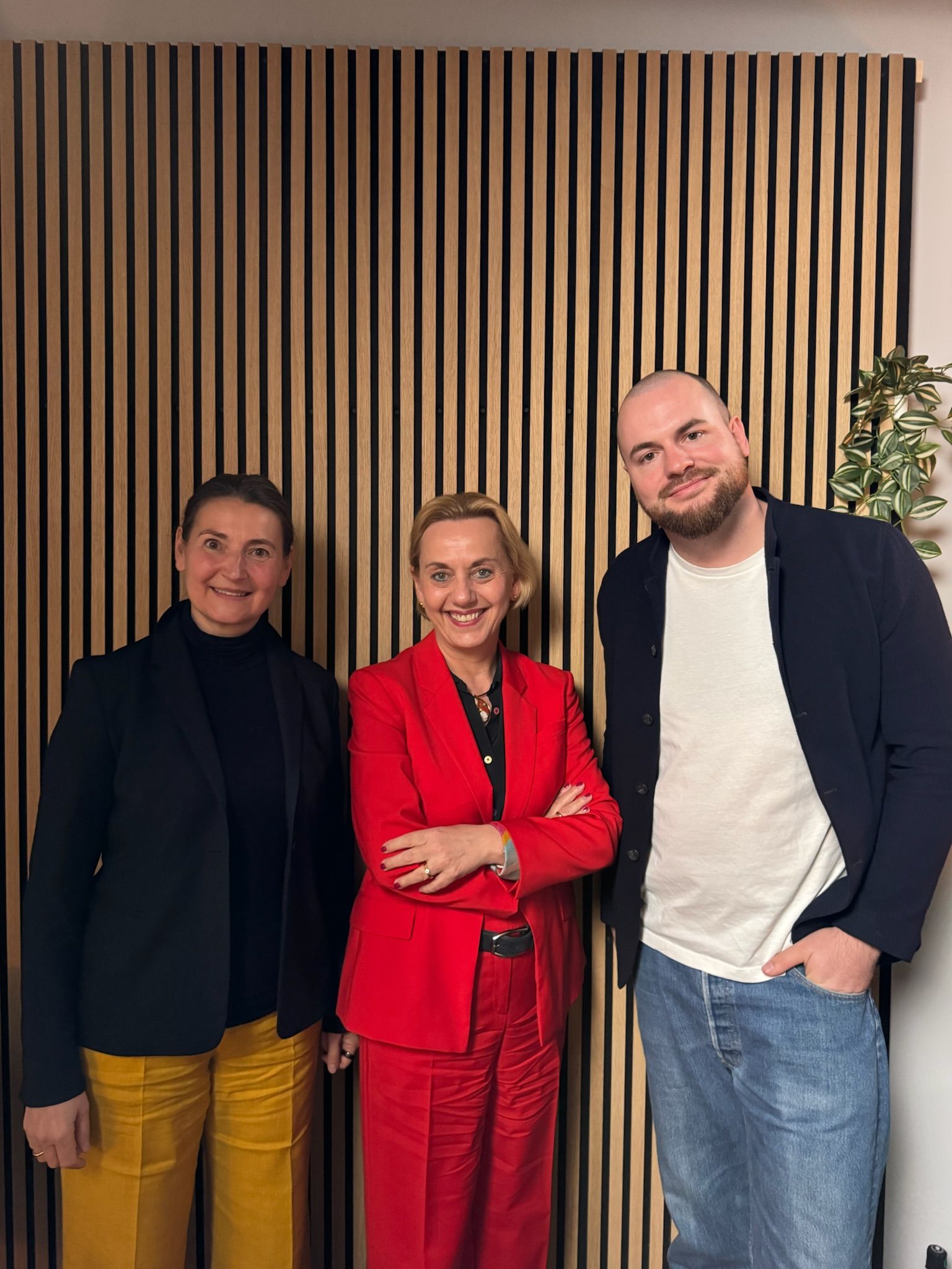 Three people standing in front of a striped wooden wall.