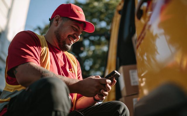 Delivery worker with phone by a van, labeled Logistics