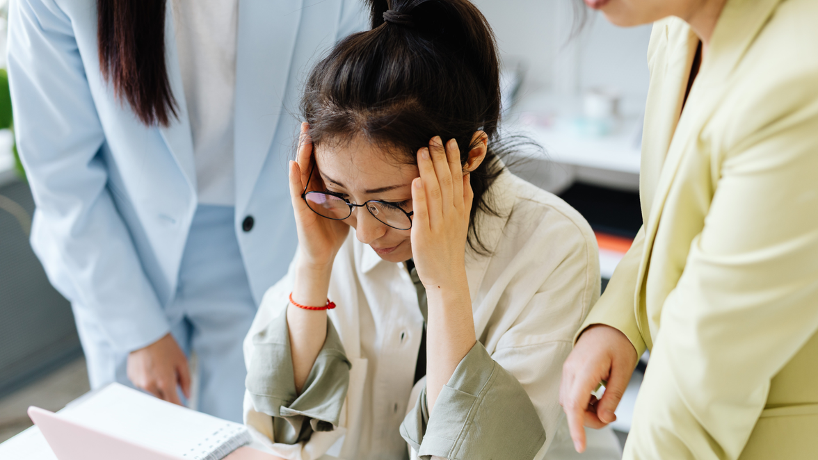 Stressed employee at desk with colleagues, highlighting need for employee comms and HR-Software tools.