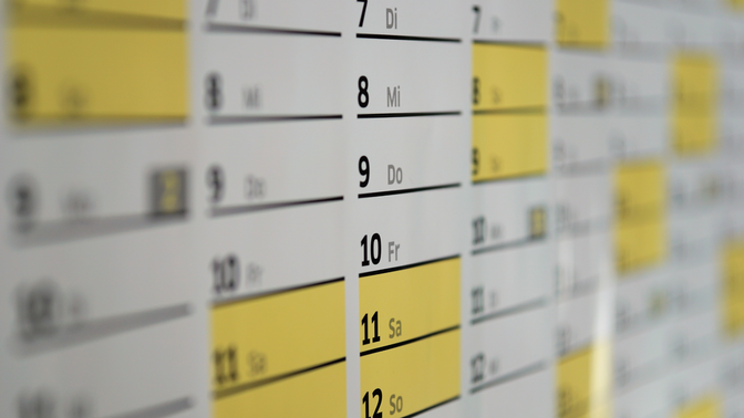 Close-up of a calendar with days and dates in black text. Yellow highlights mark specific dates. Days are labeled in German abbreviations.