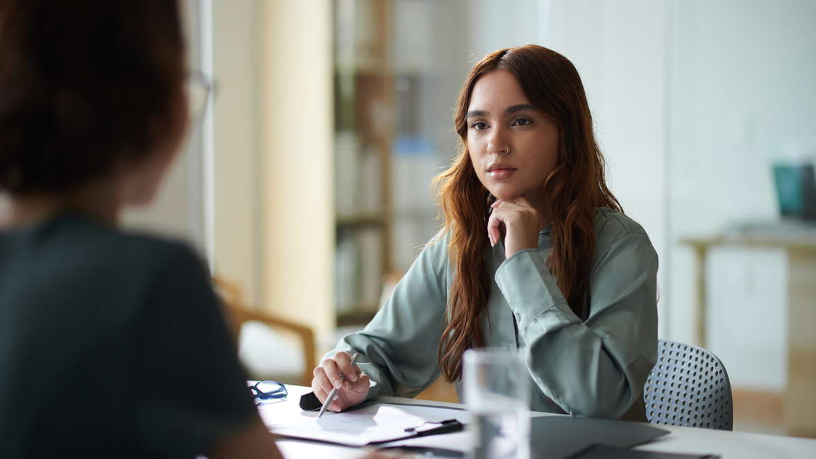 Two women in an office having an HR management discussion, paperwork and glasses on the table.