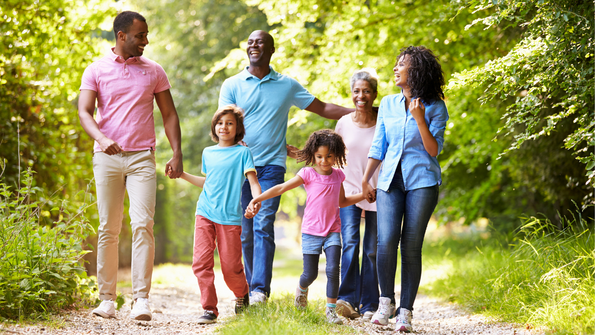 Family of six walking together on a sunny forest path, smiling and enjoying vacation time outdoors.