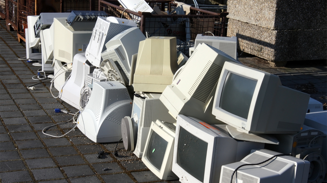 A pile of discarded CRT computer monitors and outdated electronics stacked outdoors, symbolising obsolete technology.