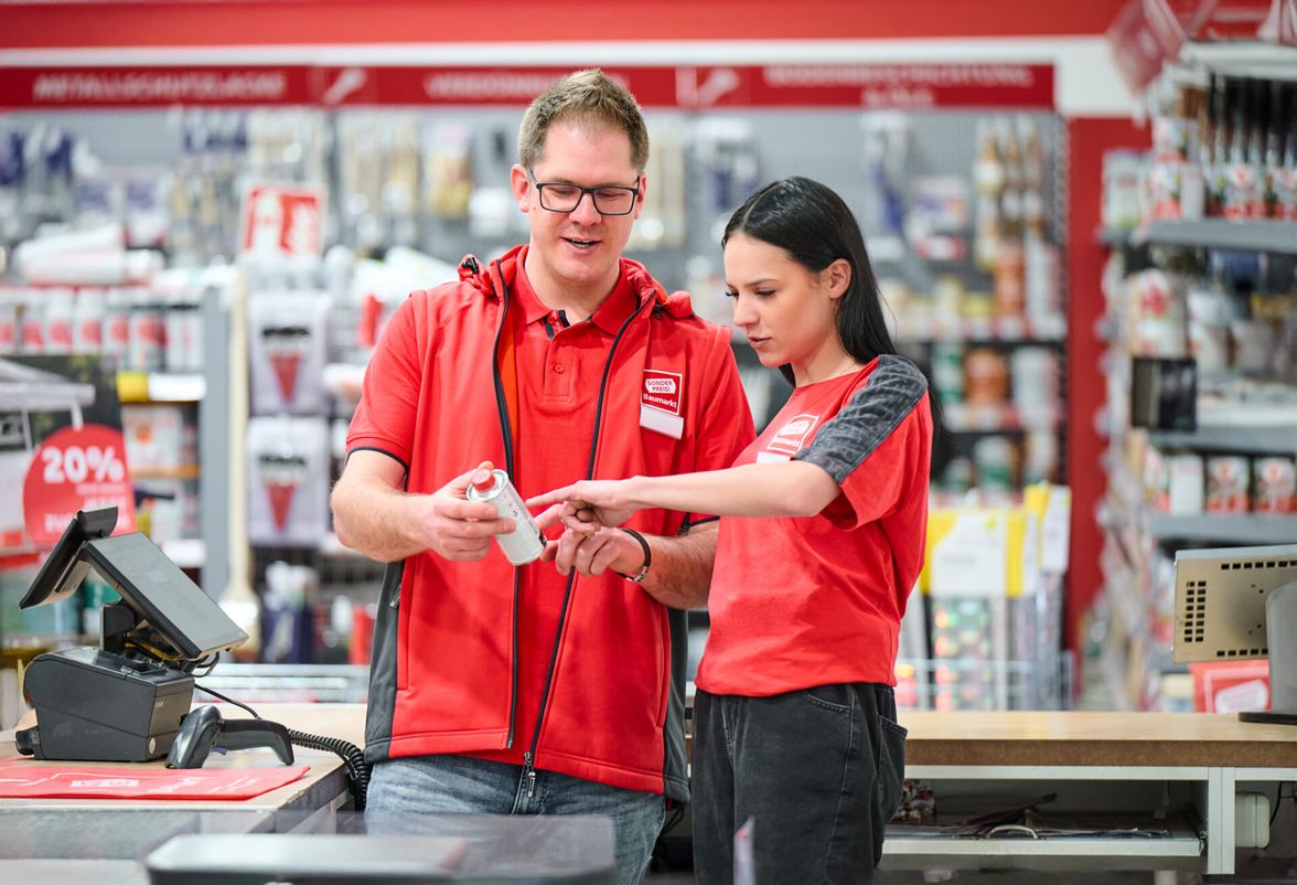 Employees in red shirts working at a register in a store.