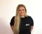 Woman with long blond hair in black EUROPART shirt standing against a plain white wall.