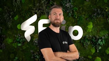 Man in black Flip shirt poses in front of green wall with large Flip logo, no UI visible.