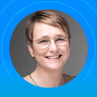 Smiling person with short hair and glasses on a blue background.