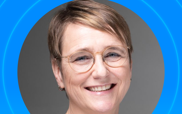Smiling person with short hair and glasses on a blue background.