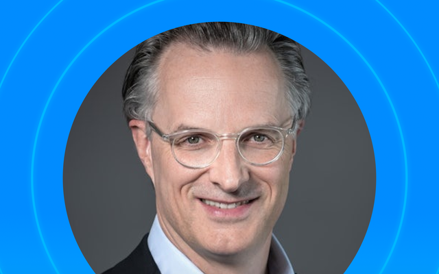 Portrait of a smiling person in a suit and glasses, set against a blue background.