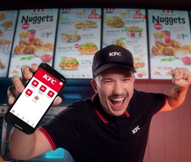 KFC employee excitedly showing a phone app at the counter.