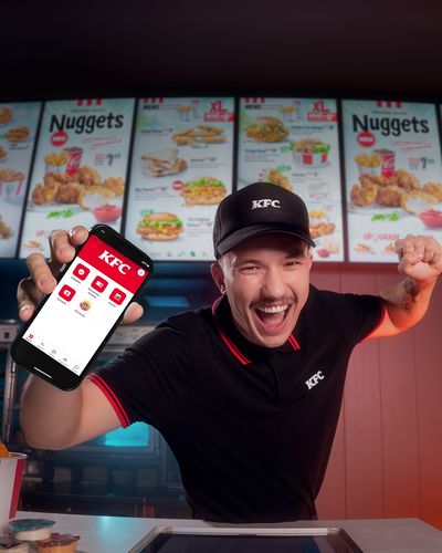 KFC employee excitedly showing a phone app at the counter.
