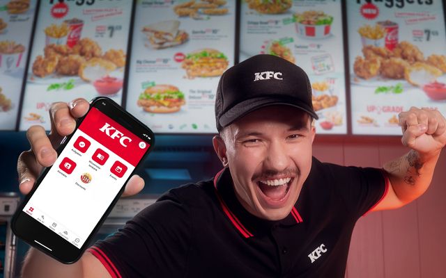 KFC employee excitedly showing a phone app at the counter.