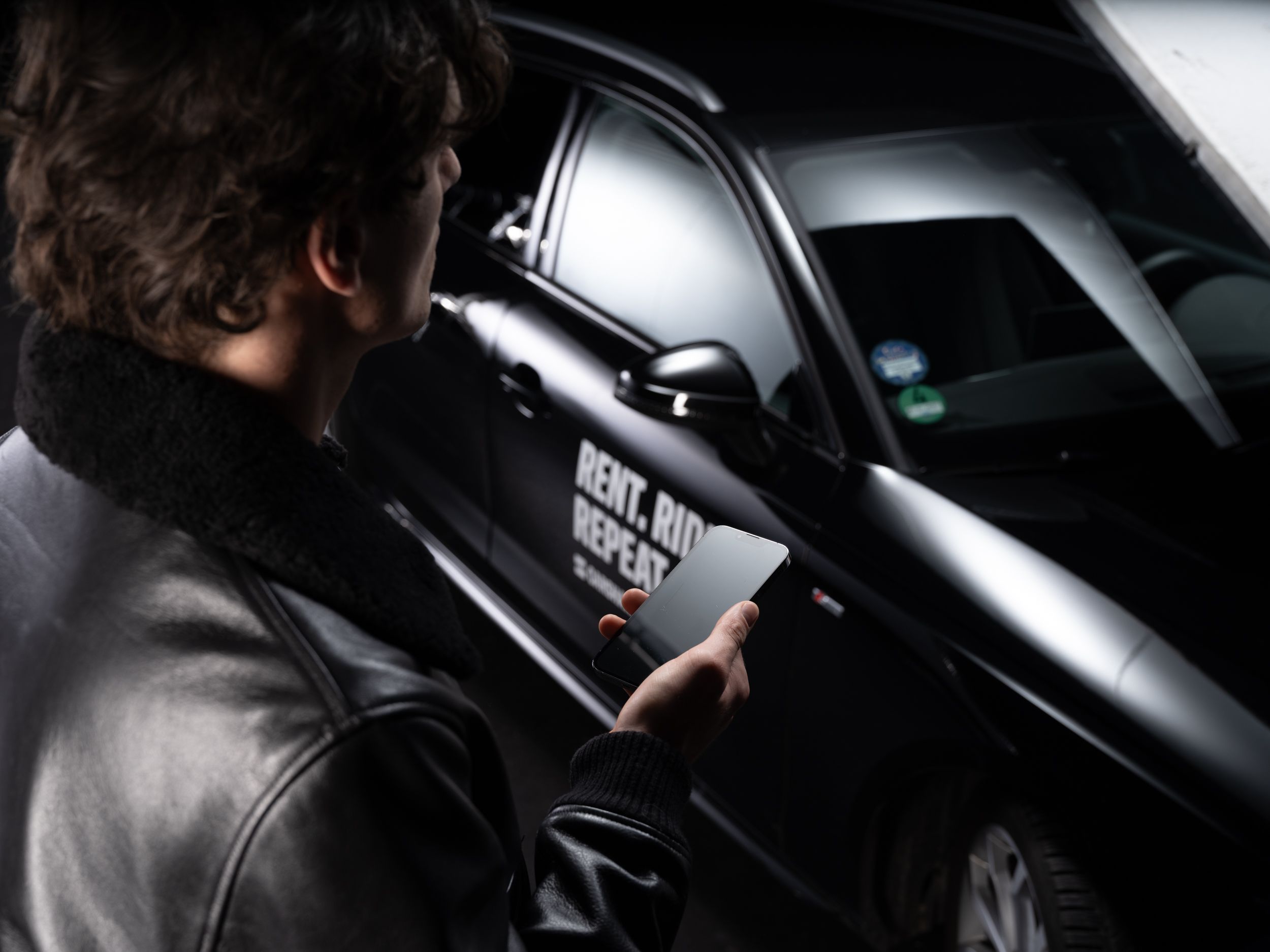 Person holding phone near car with Rent. Ride. Repeat. text.