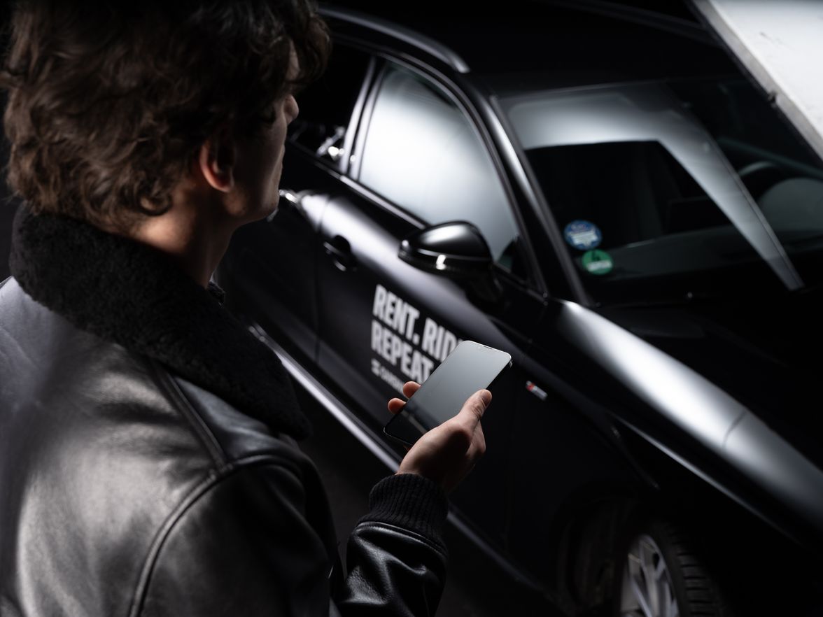 Person holding phone near car with Rent. Ride. Repeat. text.