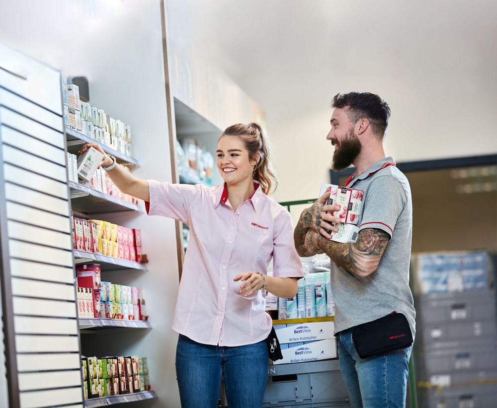 Two ROSSMANN employees stocking shelves, smiling.