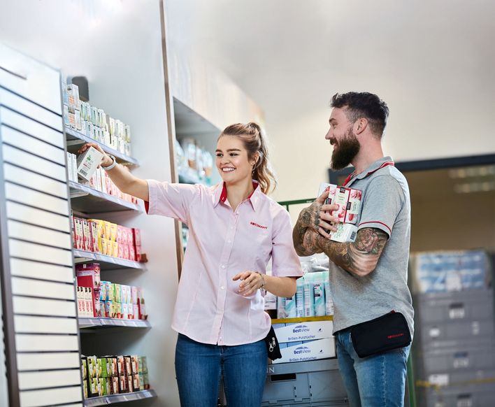 Two ROSSMANN employees stocking shelves, smiling, in a retail store environment.