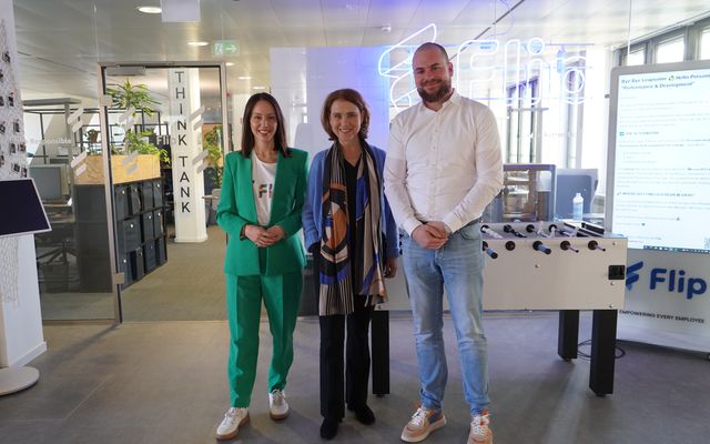 Three people stand in a modern Flip office with Mitarbeiterplattform and Employee Experience Platform visible.