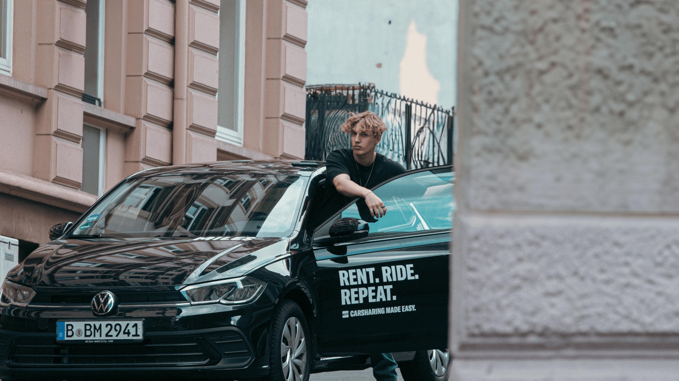 Person standing by a car with Rent. Ride. Repeat. text.