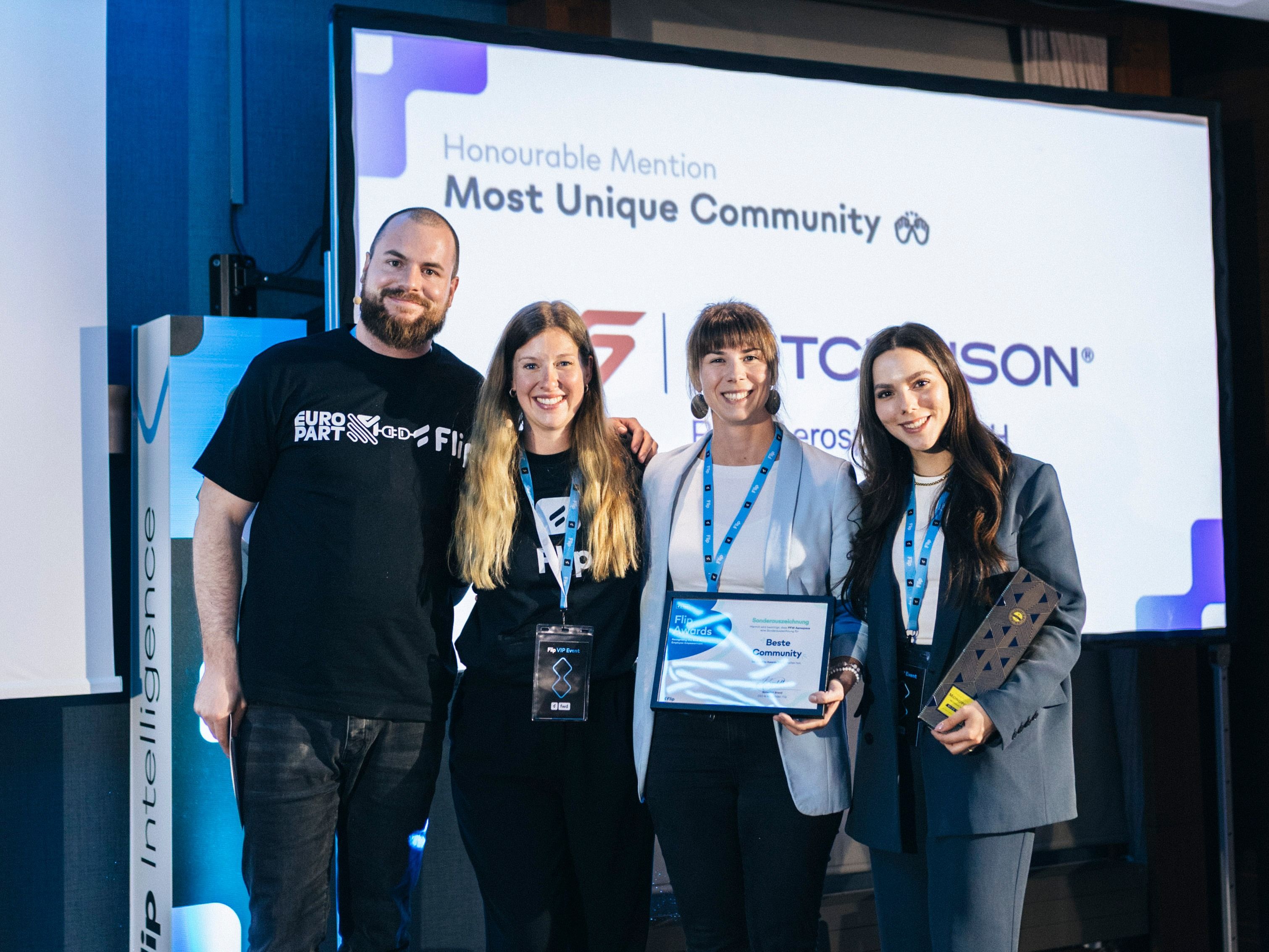 Four people at an award event; screen reads Honourable Mention Most Unique Community.