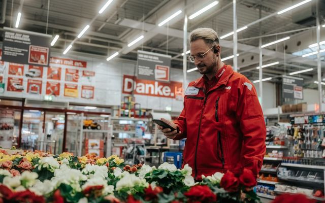 Mitarbeiter im toom-Markt nutzt digitale Mitarbeiterplattform-App, Schild: Danke. im Hintergrund.