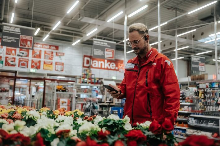 Mitarbeiter im toom-Markt nutzt digitale Mitarbeiterplattform-App, Schild: Danke. im Hintergrund.