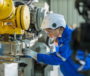 Female engineer in blue uniform and helmet operates industrial robot in a factory setting.