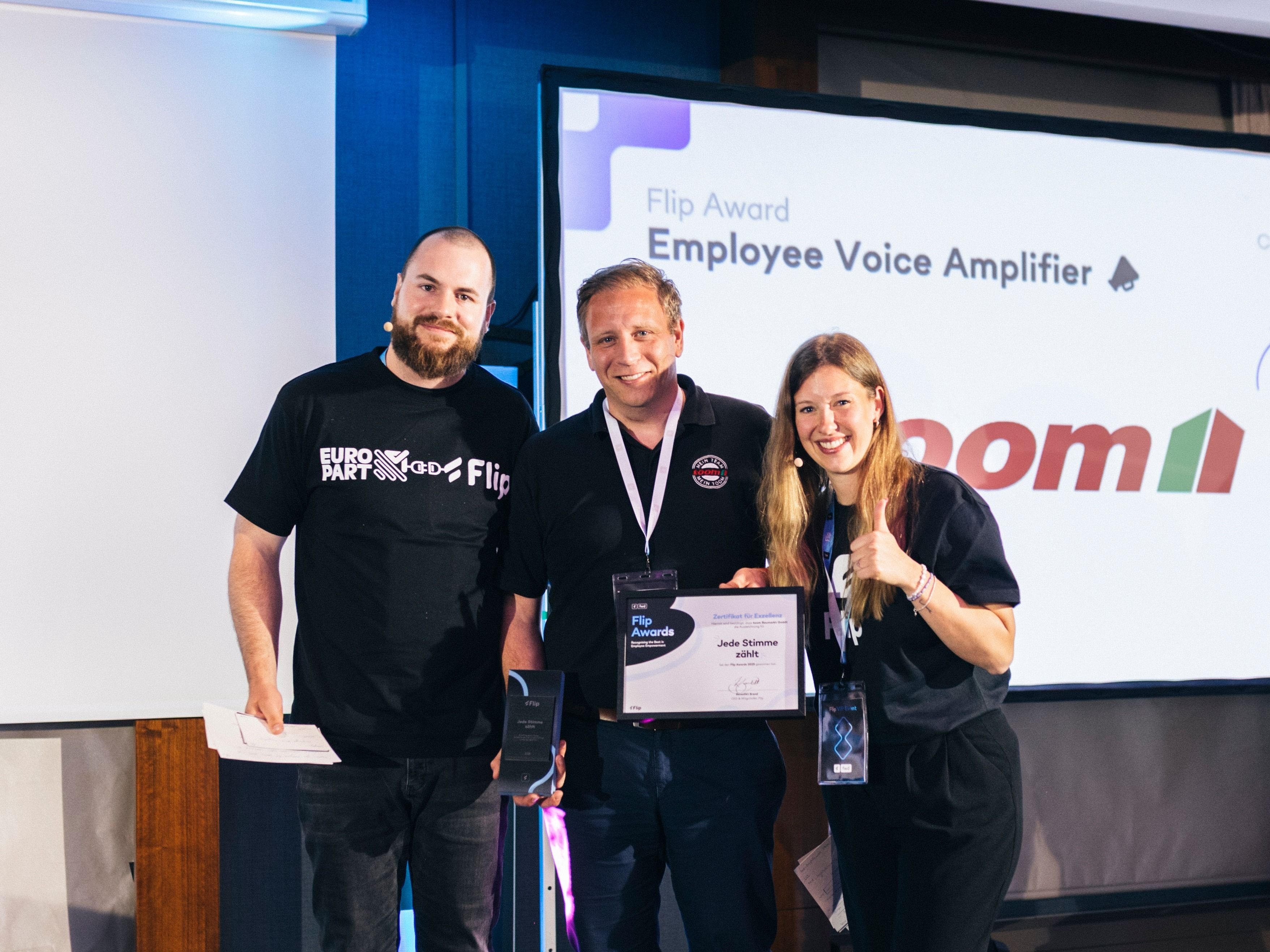 Three people on stage at Flip Award, holding Employee Voice Amplifier certificate, smiling.