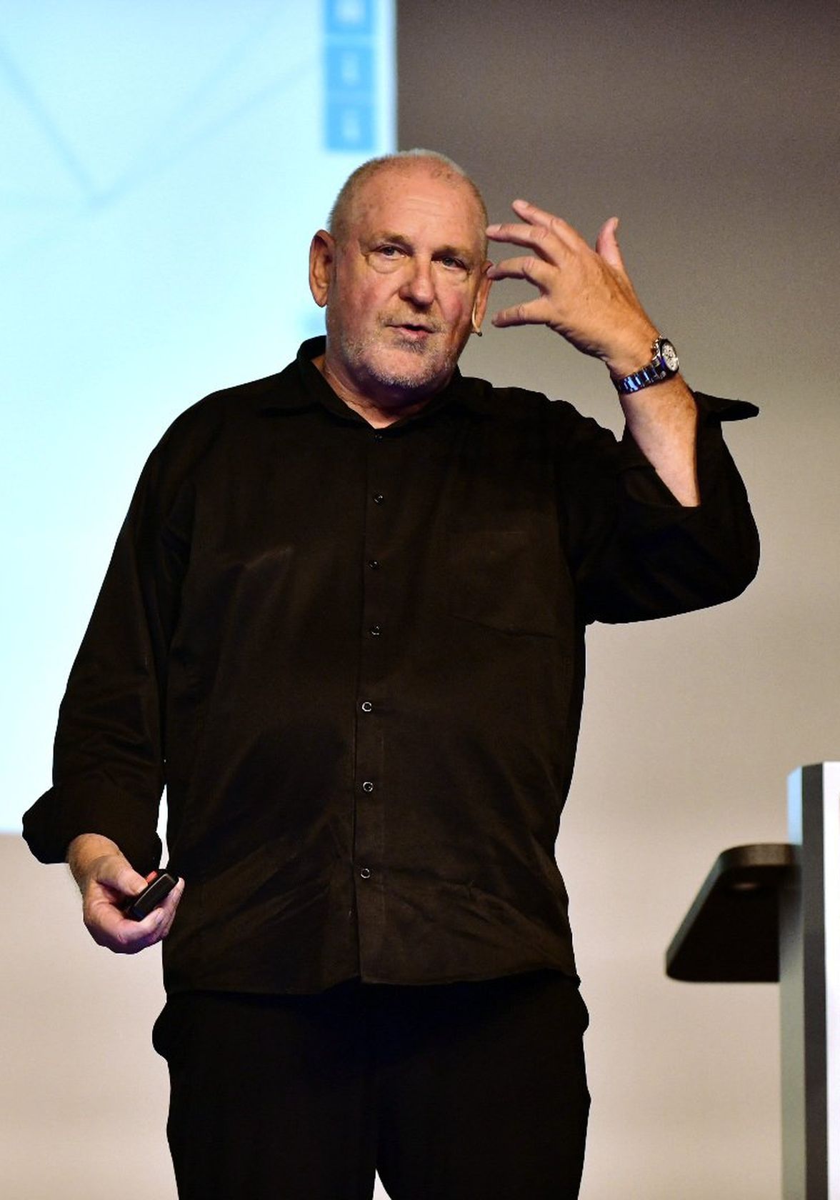 Man in black shirt gesturing on stage, giving a presentation; no visible text or UI elements.