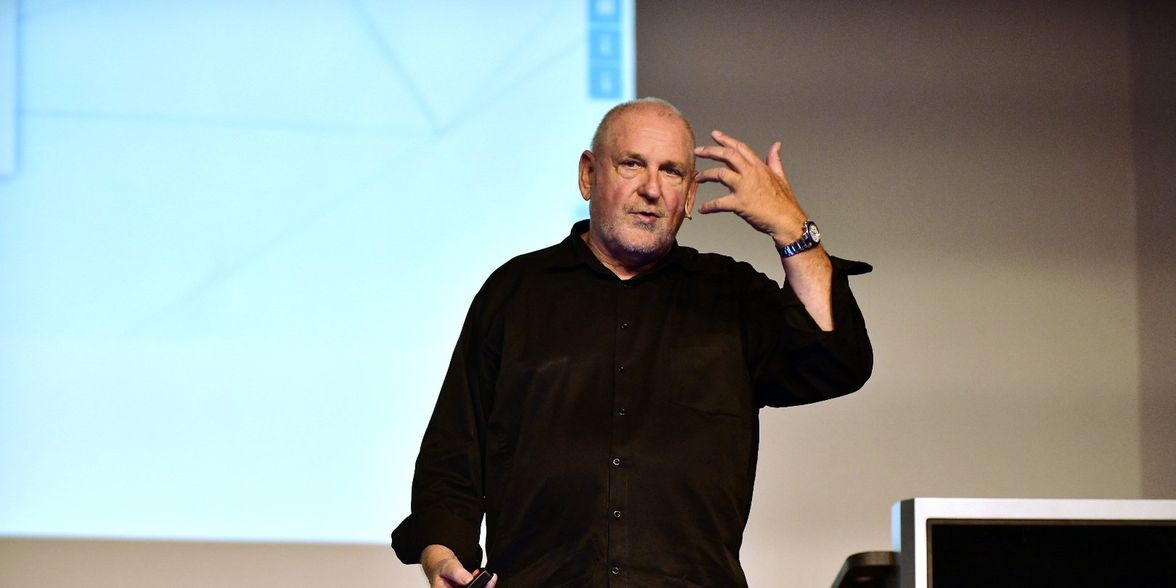 Man in black shirt gesturing on stage, giving a presentation; no visible text or UI elements.