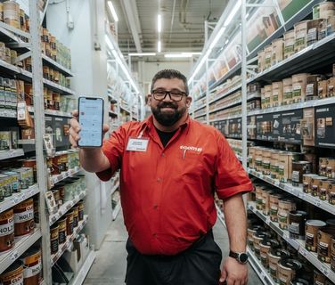 Mitarbeiter zeigt Mitarbeiter App mit Flip Flows, HR-Portal, Employee Experience Platform im Baumarkt.