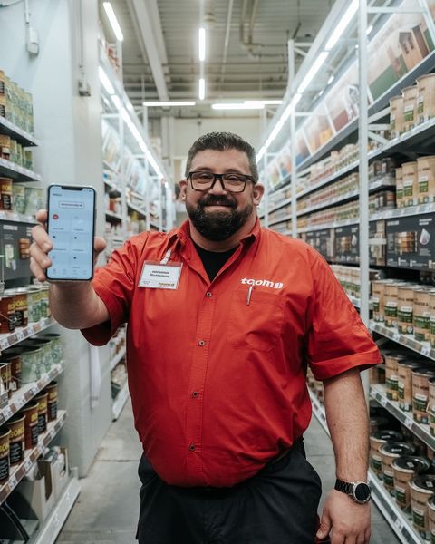 Mitarbeiter zeigt Mitarbeiter App mit Flows, HR-Portal, Employee Experience Platform im Baumarkt.