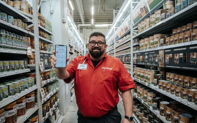 Mitarbeiter zeigt Mitarbeiter App mit Flip Flows, HR-Portal, Employee Experience Platform im Baumarkt.