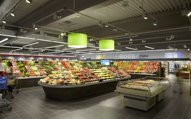 Modern EDEKA supermarket produce section with fresh fruits, vegetables, and shoppers in aisles.