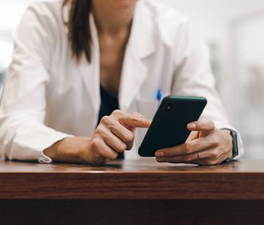Woman in healthcare uniform using smartphone, representing digital employee engagement and HR-Software.